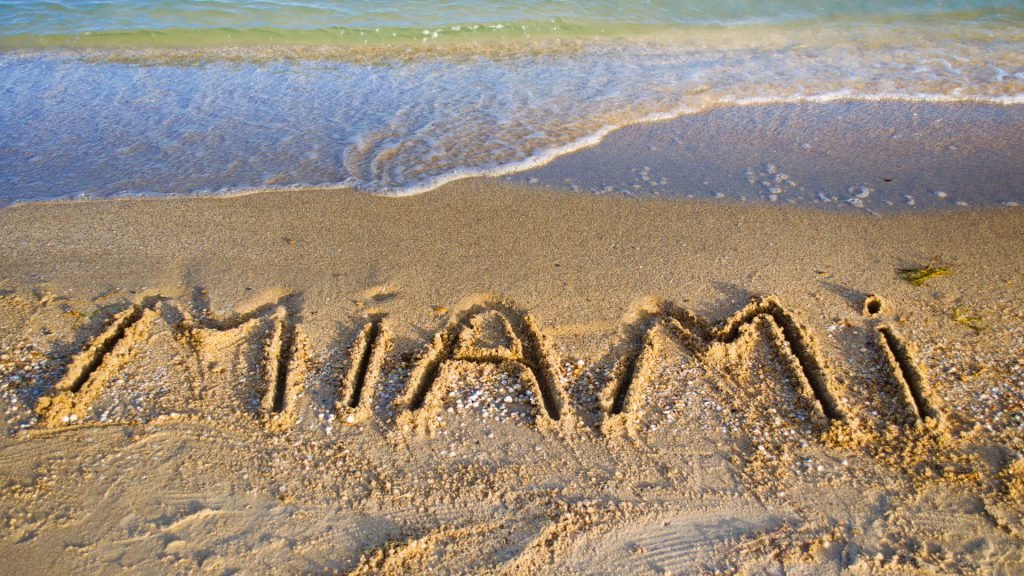 Palabra 'Miami' escrita en la arena de la playa, representando el mundo de los agentes inmobiliarios con LUZ ANGELA AGREDO - Agente Inmobiliaria en Florida
