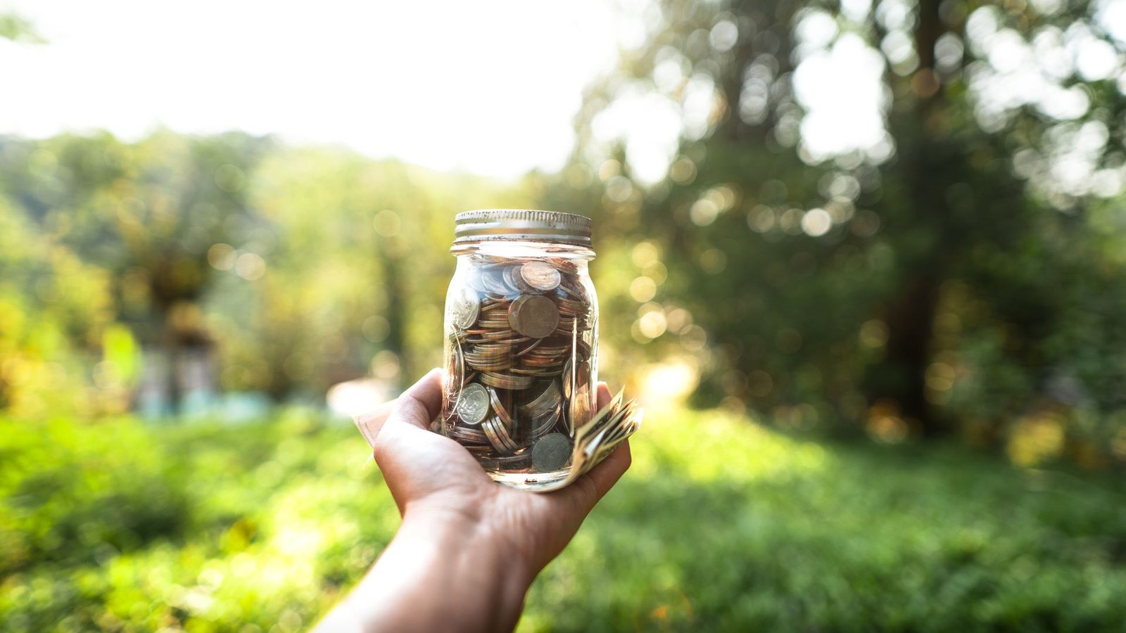 Manos colocando monedas y billetes en un frasco de ahorros